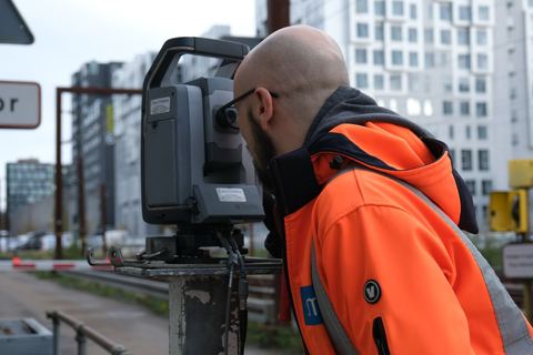 SMT-medarbejder sigter gennem en totalstation ved en byggeplads mellem nye boligblokke